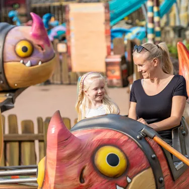 Eine Frau und ein Mädchen sitzen in der Gondel von Grobians Wolkenspringer im Heide Park Resort. Die Gondeln sind bunte Drachen.