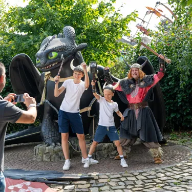 Ein Mann macht ein Foto von Ohnezahn , einem Wikinger und zwei verkleideten Jungs im Heide Park Resort.