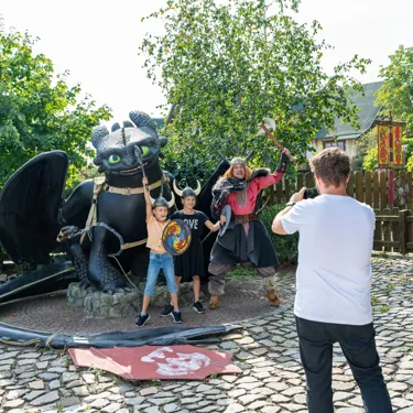 Ein Mann macht ein Foto von Ohnezahn , einem Wikinger und zwei verkleideten Mädchen im Heide Park Resort.